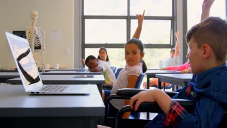 Schulkinder-Heben-Die-Hand,-Während-Sie-In-Der-Grundschule-Am-Schreibtisch-Sitzen,-4k