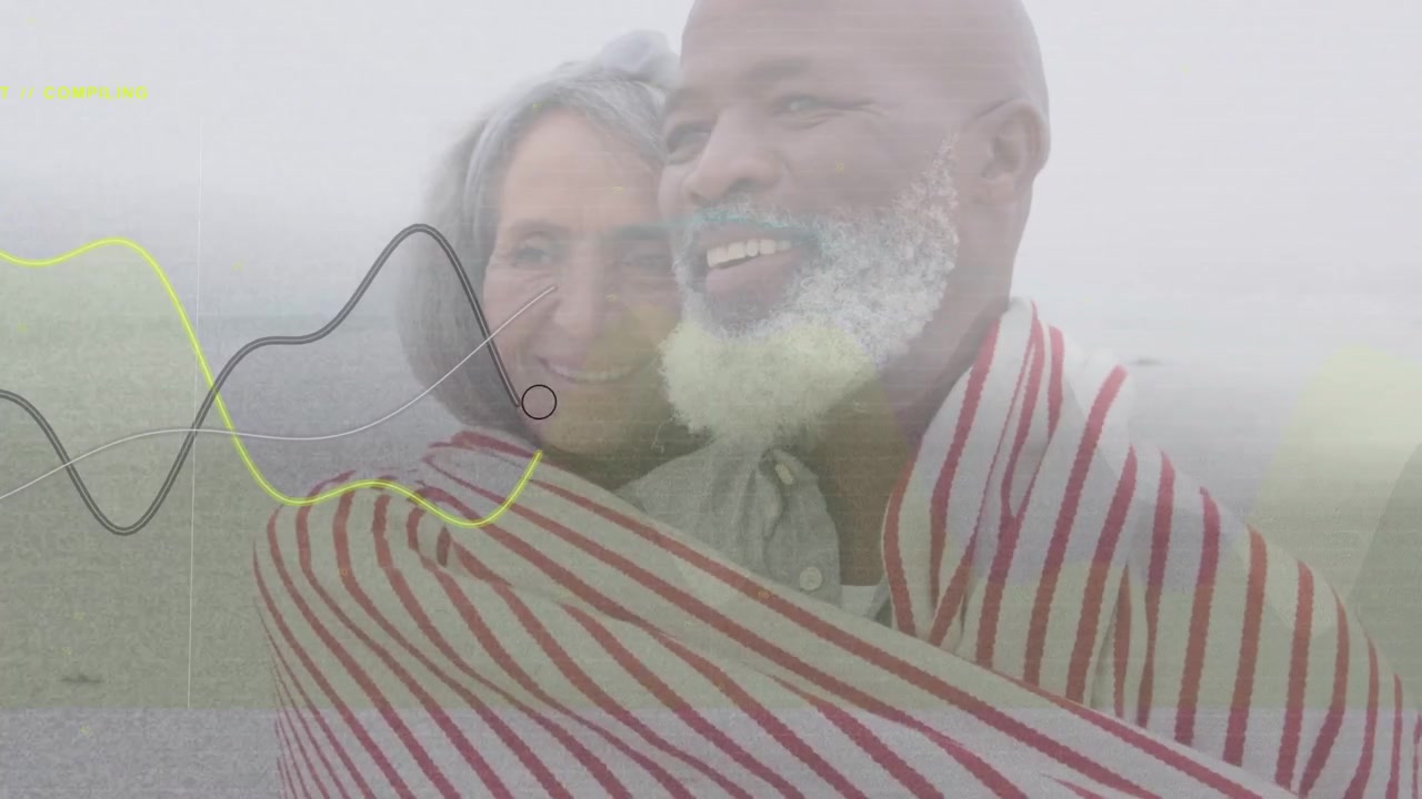 Pareja madura en la costa, el hombre riendo, tirando de una manta para abrigarse, con texto de marcador tecnológico cruzando los rostros.