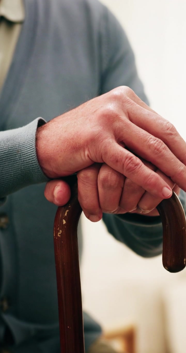 Persona anziana con le mani appoggiate su un bastone da passeggio in legno