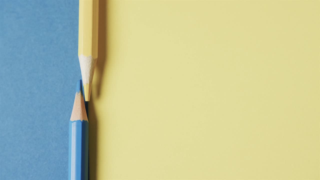 primer plano de lápices de colores amarillos y azules con espacio de copia en fondo azul y amarillo, en cámara lenta