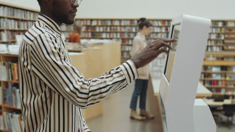 hombre afro usando una pantalla digital interactiva en la biblioteca