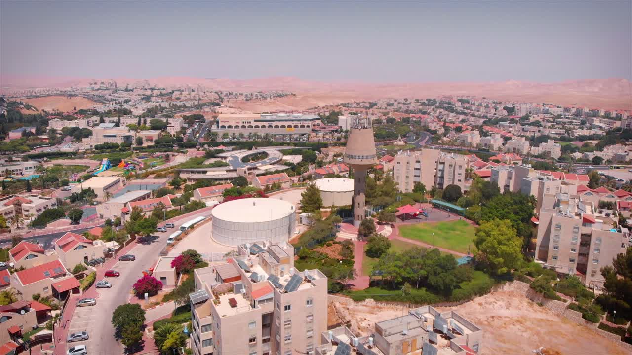 Aerial view of a town with a prominent water tower and reservoir, surrounded by residential buildings and distant desert mountains