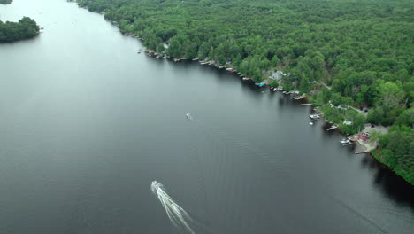 Aerial-video-of-a-boat-traversing-the-water-with-a-skier,-high-altitude,-Burrillville,-RI