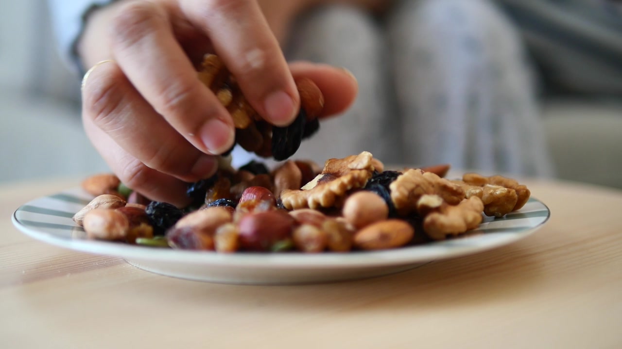Hand Picking Mixed Nuts and Dried Fruits from a Plate