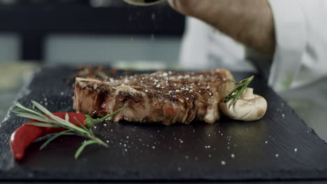 chef peppering grilled meat at cut board. man hands pepper steak in slow motion