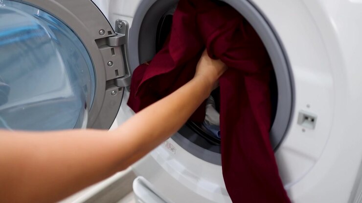 A person loads dirty clothes into a front-loading washing machine and closes the door.