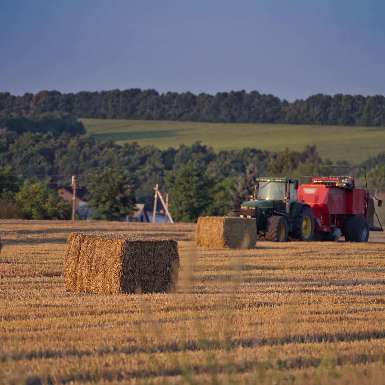 Square bales and a tractor on the field. agricultural machine pressing dry hay on the natural rural landscape in summer.