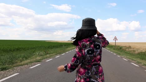 rear view of a woman in floral dress and hat walking on remote asphalt road