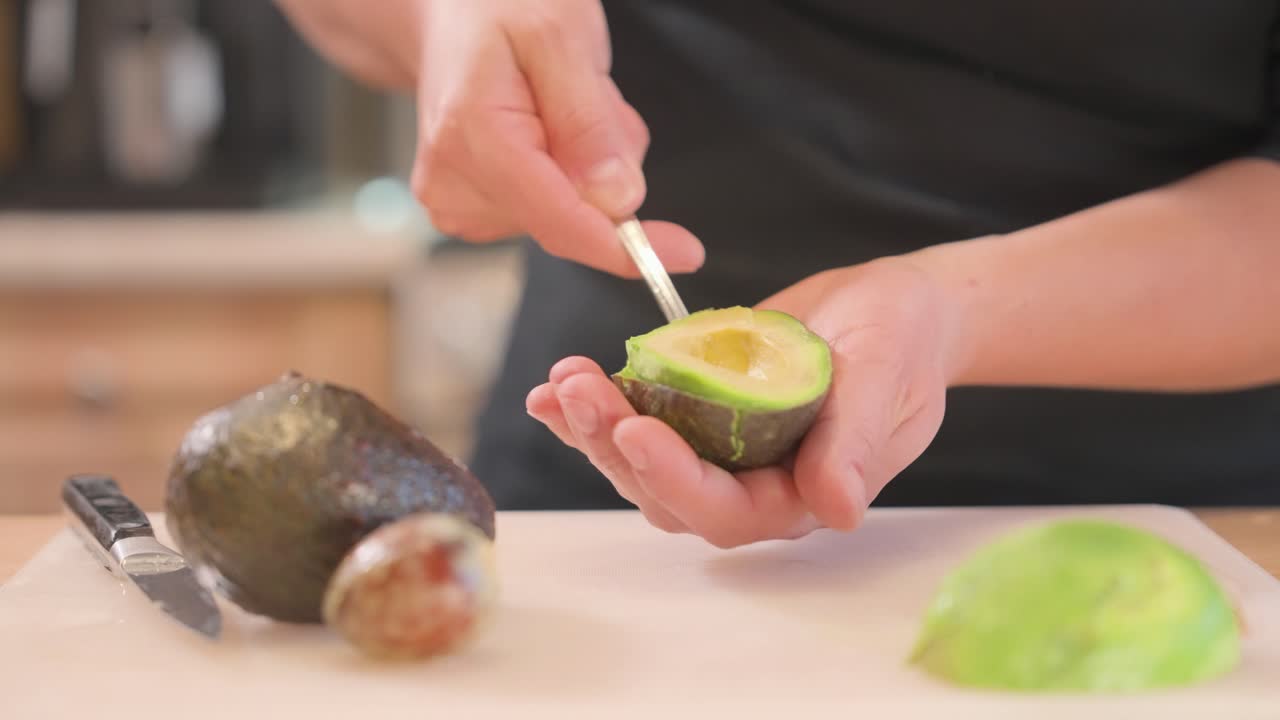 An at-home cook uses a spoon to scoop out half an avocado.