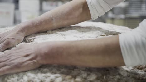 close up shot of men hands of a baker spreading flour evenly on a dough for sweets in a sweets factory in medina sidonia