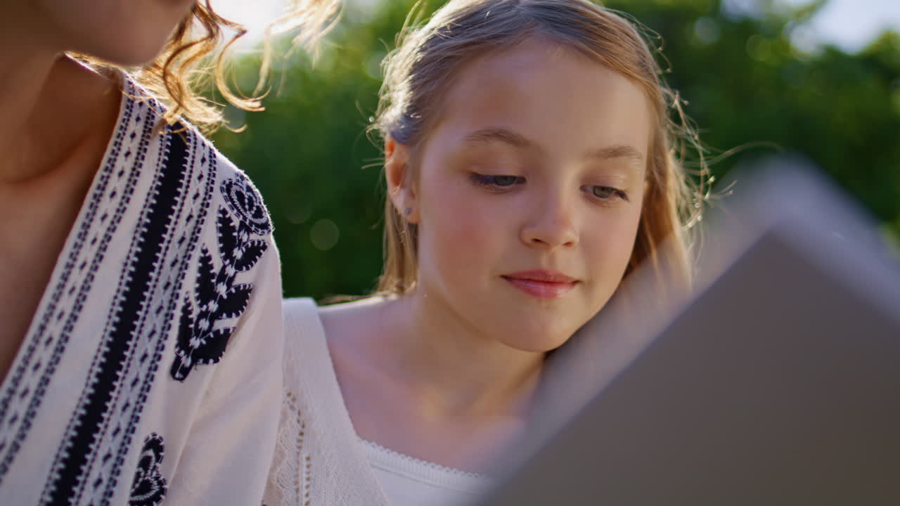 Summer child reading book with mom resting together at weekend picnic closeup
