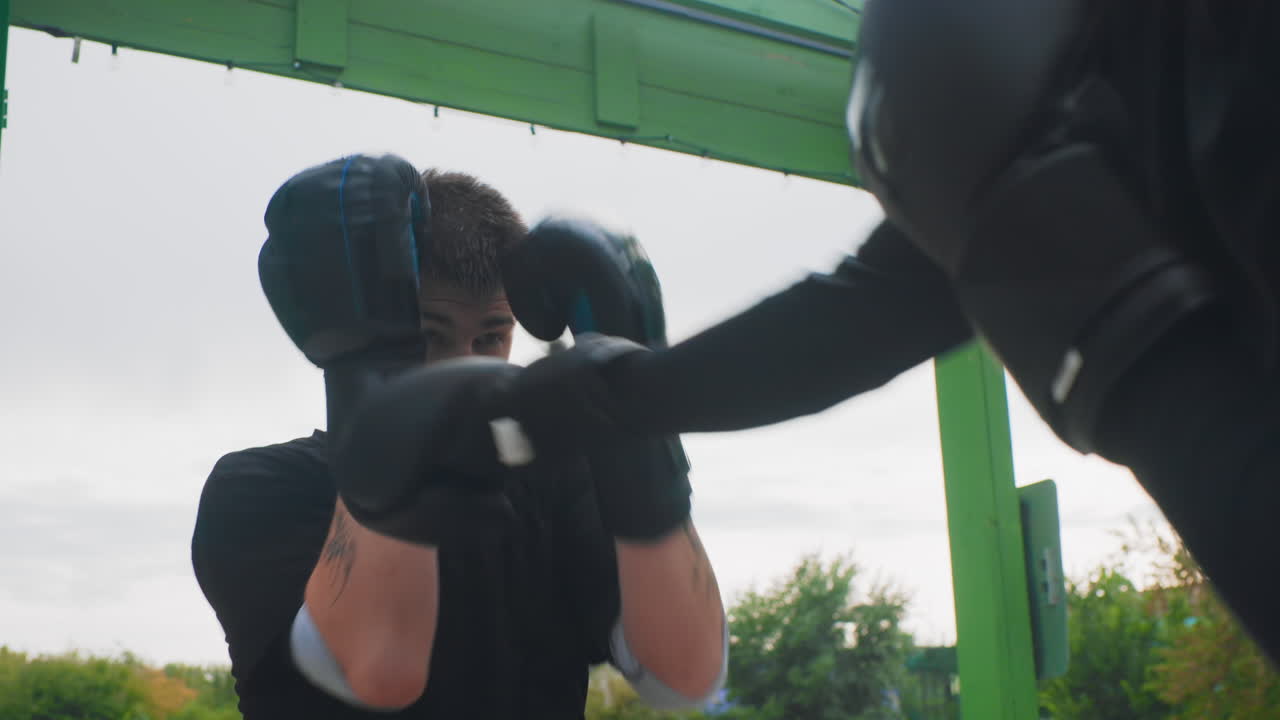 Boxeador joven y enérgico entrenando vigorosamente con movimientos hábiles de pies y defensa. Boxeador blanco joven y dinámico participando en un entrenamiento intenso al aire libre con golpes rápidos y maniobras defensivas.