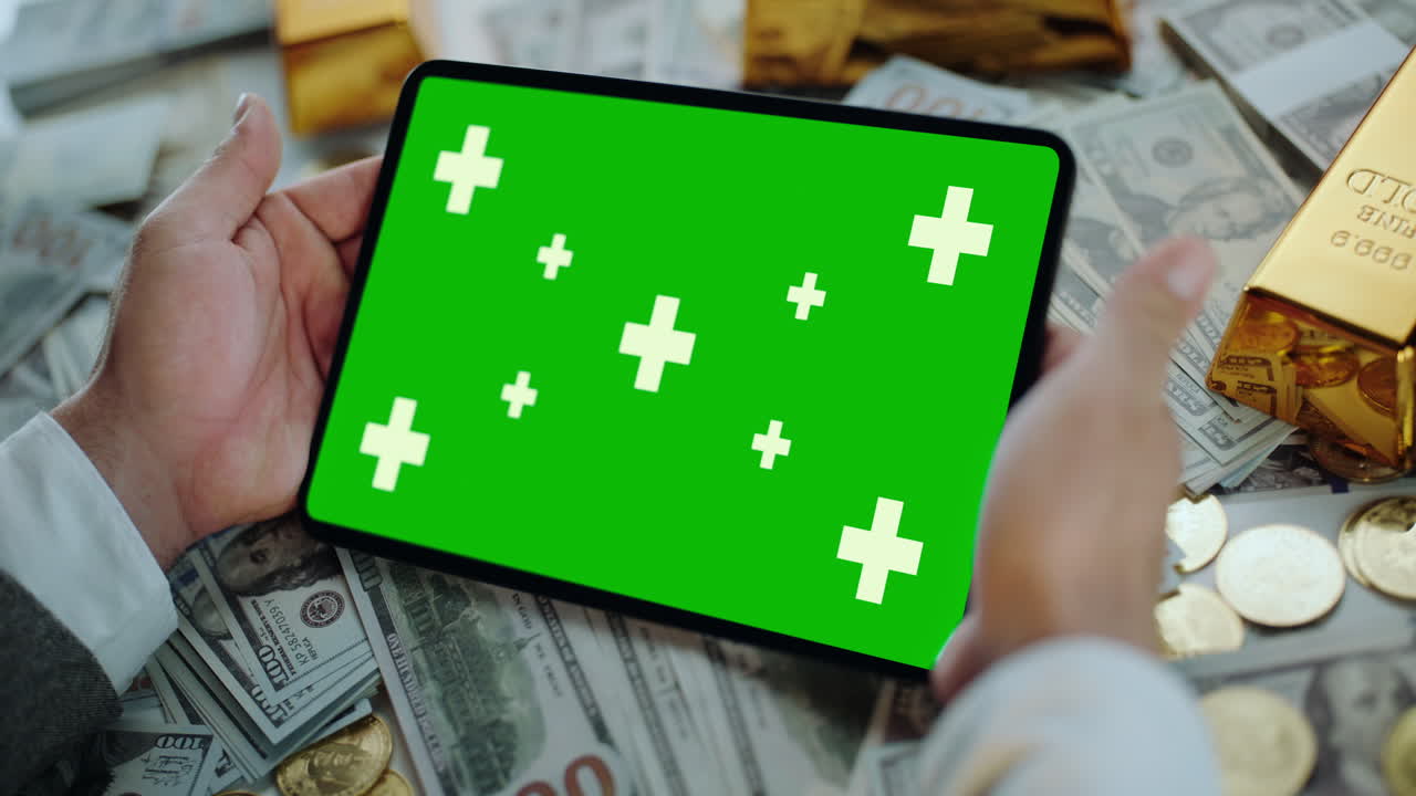 Tablet with Green Screen Surrounded by Money and Gold