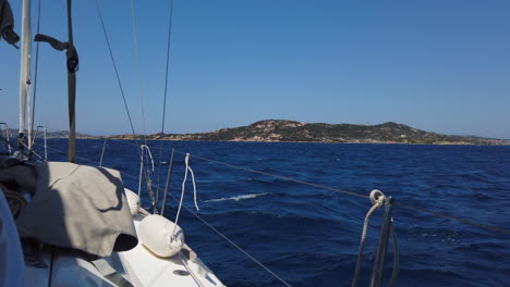 wide shot from a sailing boat, cruise in deep blue water with a island in the background, sardegna, italy