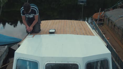 joven pinta la mitad de la cabina de la timonera de un barco de madera con imprimación