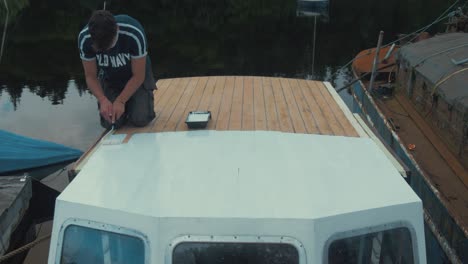 young man paints half of wooden boat wheelhouse cabin with primer