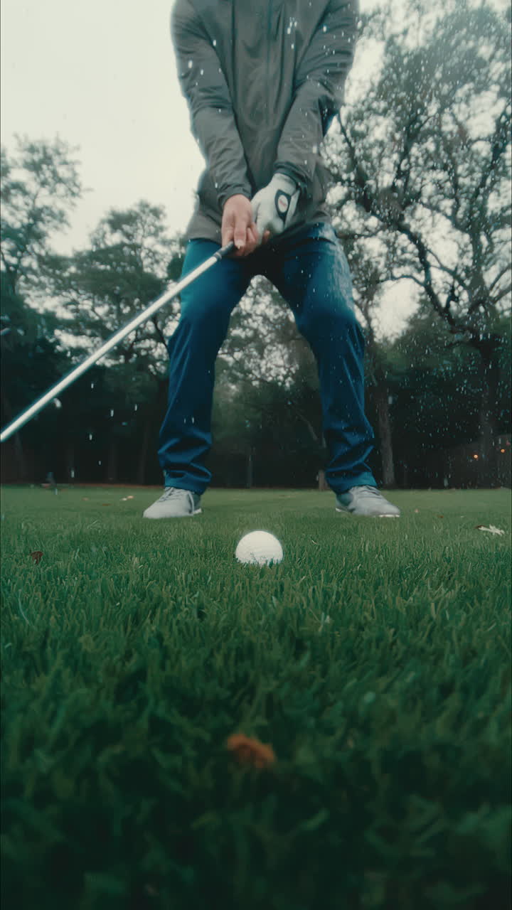 golfista masculino se encuentra en el fairway en lluvia, columpios y fichas bola de golf en cámara lenta y salpicaduras de agua en todas partes