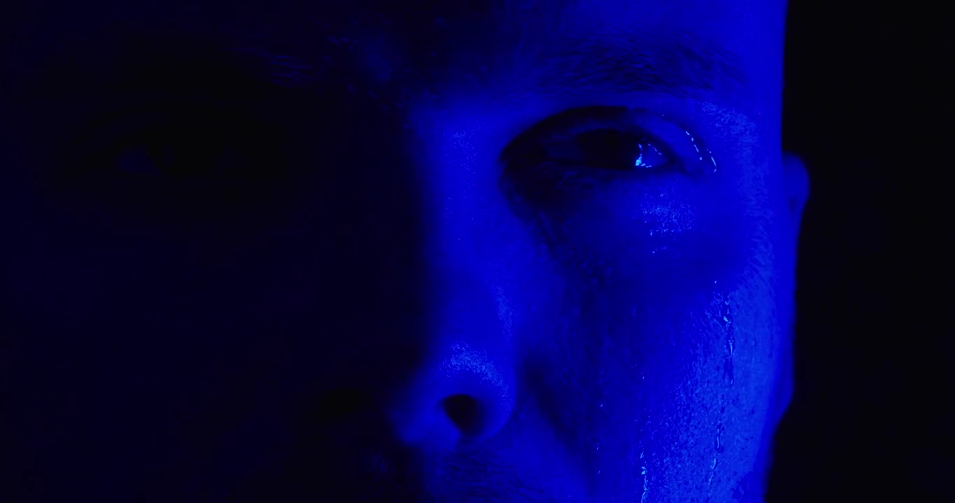 Primo piano di un uomo emotivo con lacrime sul viso illuminato da luci rosse di emergenza. Concetto di dolore, tristezza, disagio emotivo, presenza della polizia ed emozioni umane drammatiche