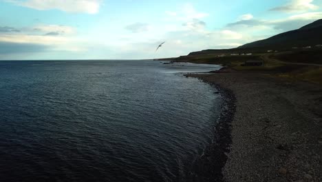 Aerial-landscape-view-of-Iceland-north-coastline,-with-ocean-waves-crashing-on-the-shoreline,-at-dusk