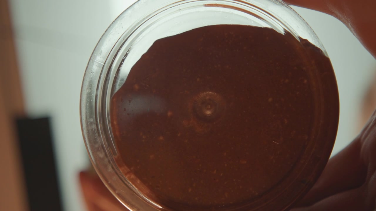 Filling jar with syrupy chocolate and smooth texture. Pantry view featuring chocolate jar being filled and sealed. Visual of glass container being filled with glossy chocolate and sealed with lid