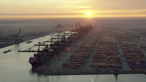 sun rises over container port with loading carts prepping the vessels to be loaded
