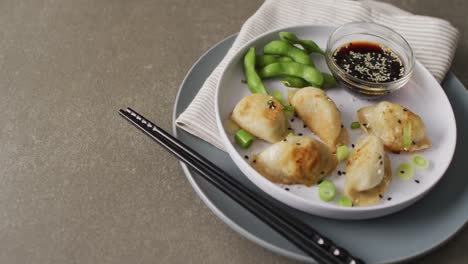 composition of plate with gyoza dumplings and soy sauce with chopsticks on grey background