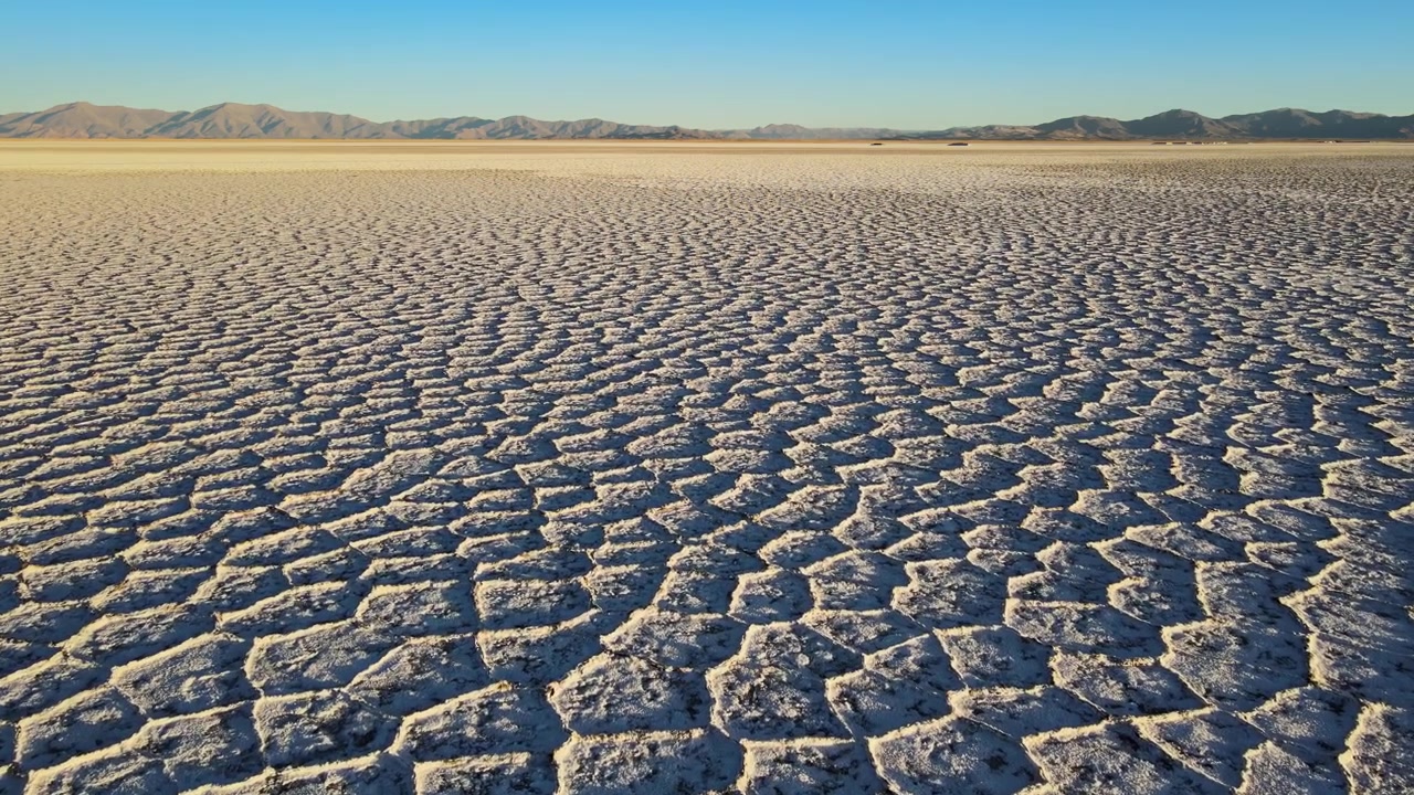 Polígonos de sal rachados estendem-se pelas Salinas Grandes em direção às distantes montanhas andinas sob a luz clara da tarde, útil como um plano de estabelecimento de paisagem desértica ampla