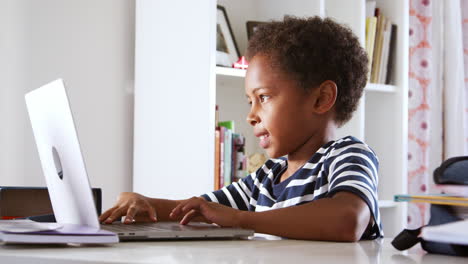 Young-Boy-Sitting-At-Desk-In-Bedroom-Using-Laptop-Computer