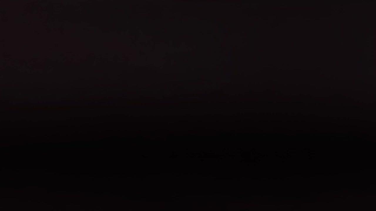 A red cricket ball moves across a dark background, showcasing its seam and rotation.