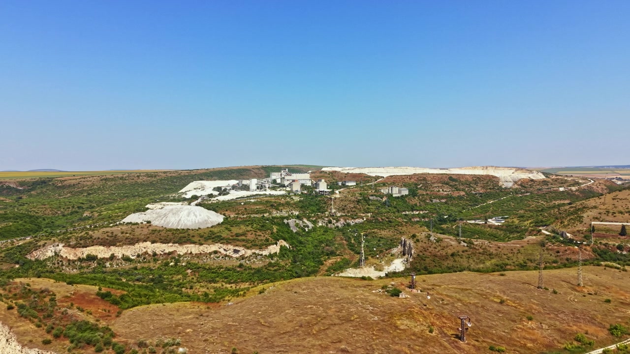 Large industrial site in a rural area with trees and hills under a clear blue sky
