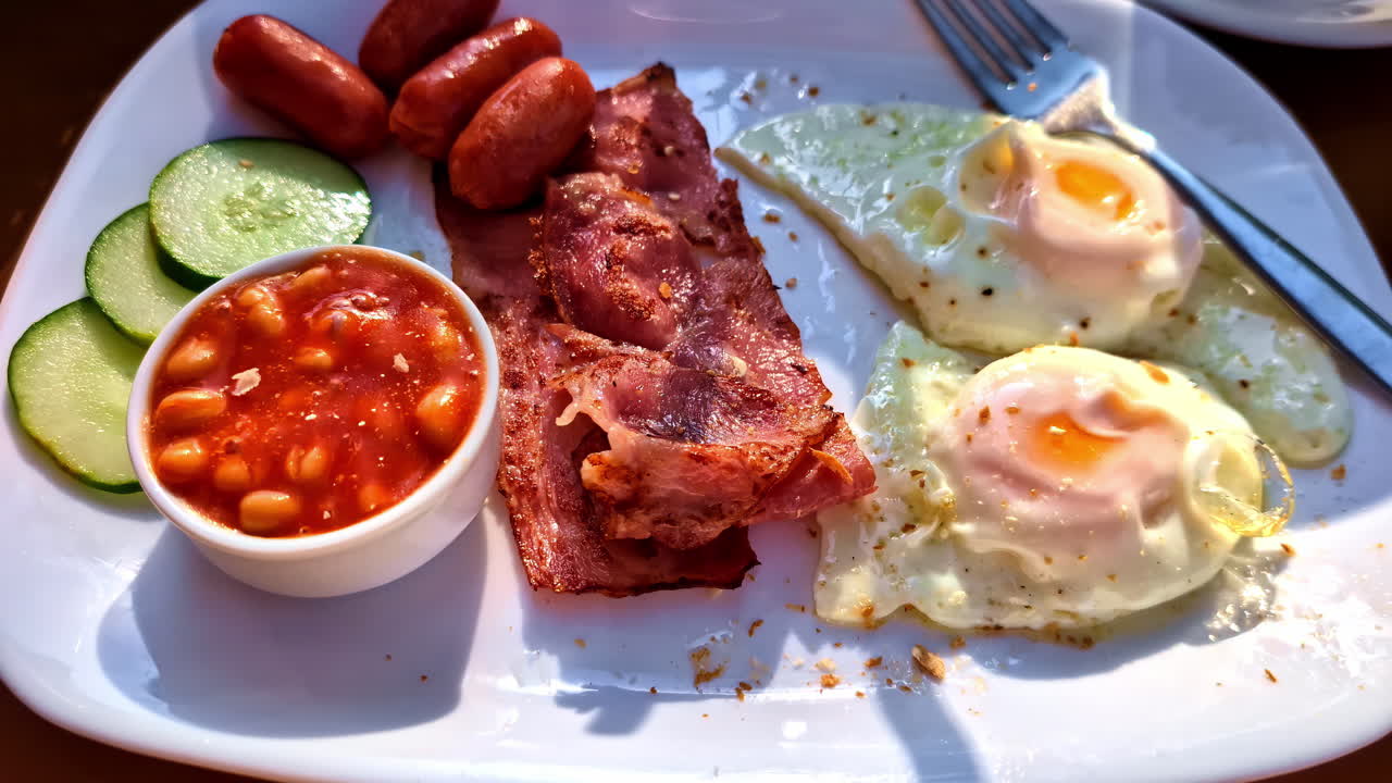 Continental breakfast on plate, eggs bacon beans cucumber and sausage