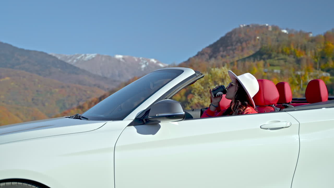 경치 좋은 산악 도로 여행 에서 컨버터블 자동차 에서 커피 휴식을 즐기는 여자