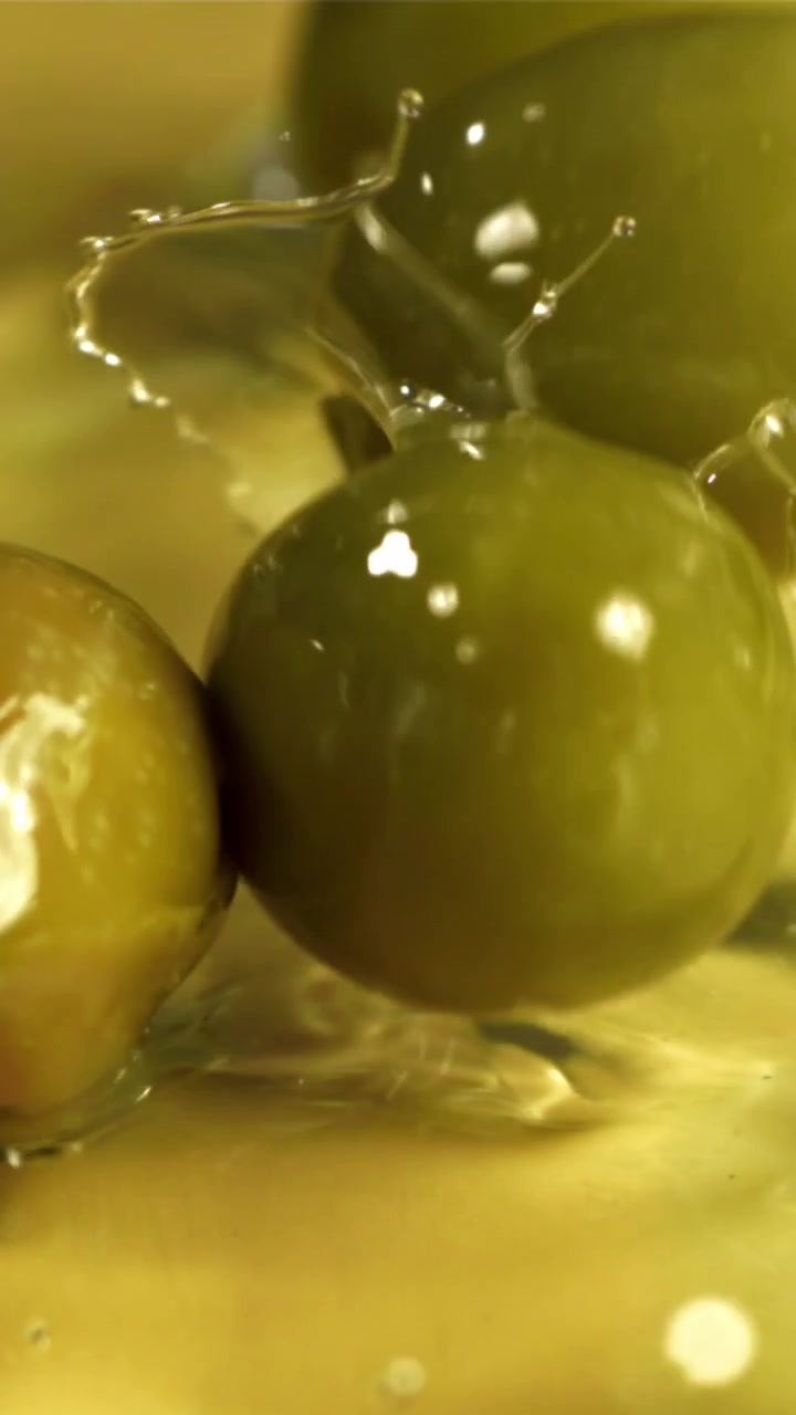 Olive verdi che schizzano in olio d'oliva dorato al rallentatore