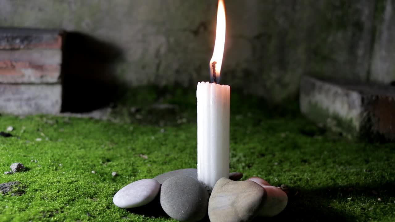Candle on base of green moss with base surrounded with small pebbles