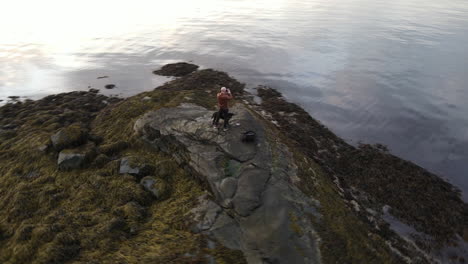 aerial footage circling around a man standing at the shore in trondheim, norway and taking pictures with a camera