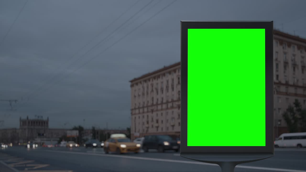 Cartellone pubblicitario moderno con schermo verde su una trafficata autostrada cittadina sfocata con traffico.