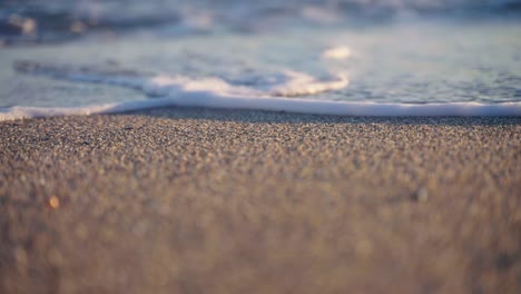 Centrarse-En-Los-Granos-De-Arena-En-La-Playa-Con-Ondas-De-Cámara-Lenta-En-El-Fondo