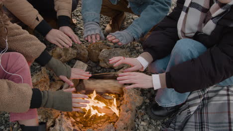 카메라는 모닥불 근처의 십대 그룹의 손에 초점을 맞춥니다.