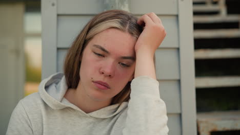 close-up of young lady resting her head on hand with pensive expression, showing deep contemplation, soft sunlight creates warmth in background