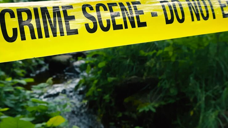 Ripresa ravvicinata di un nastro giallo della polizia "non oltrepassare" teso sopra e davanti a un piccolo ruscello o fiume nella natura verde che scorre tra le rocce in estate