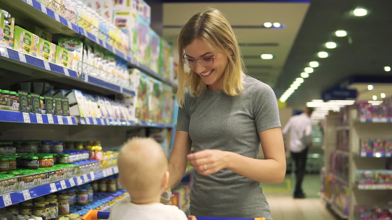 mujer joven atractiva con hija linda en el carrito de compras la elección de productos en la sección para niños en el supermercado. el niño