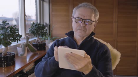 Middle-aged-caucasian-man-is-looking-for-information-on-a-tablet-in-a-hobby-room-near-a-window-with-plants