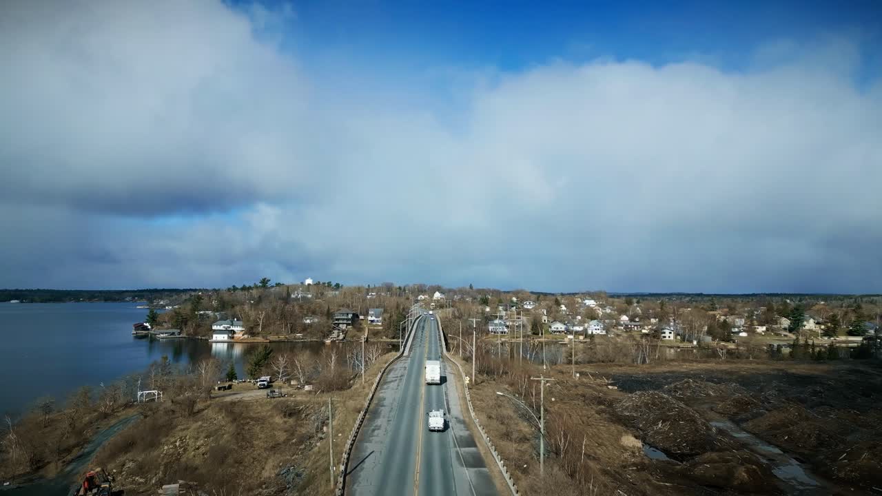 белый грузовик проезжает по возвышенному озерному мосту в сельской местности.
