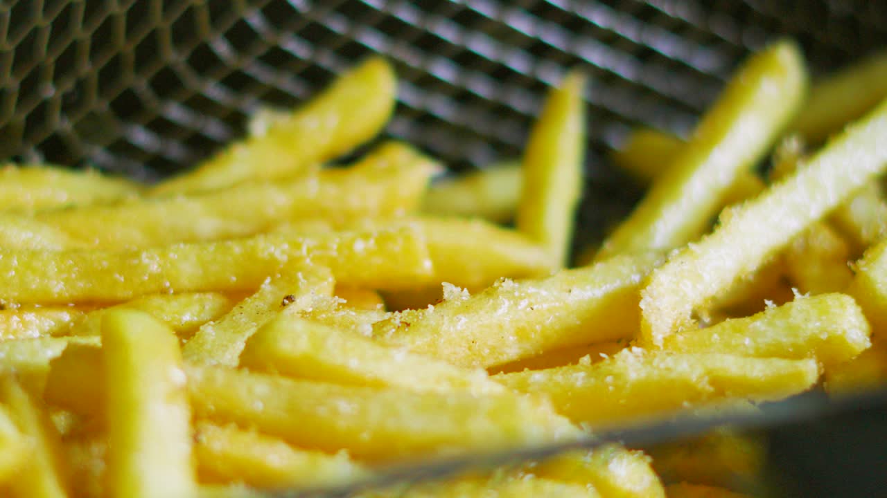 French Fries Rising from Deep Fat Fryer Basket in Slow Motion Ready to Serve After Cooking in Bubbling Hot Oil. Unhealthy Crispy Chips Fast Food