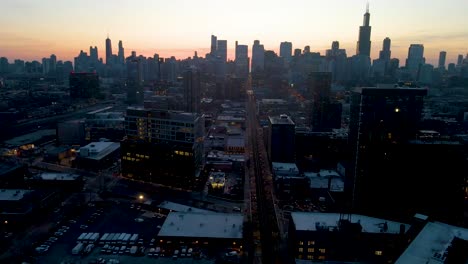 A-captivating-drone-aerial-view-of-a-Chicago-at-dusk,-showcasing-illuminated-skyscrapers-against-the-darkening-sky-The-golden-hues-of-sunset-paint-a-serene-backdrop,-highlighting-architectural-marvels