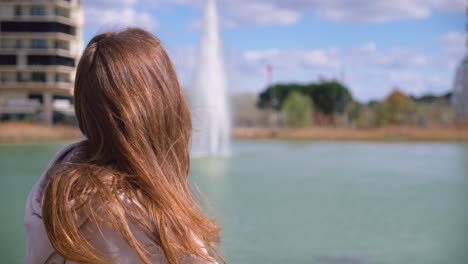 Schöne-Brünette-Frau,-Die-Sonnigen-Tag-Genießt-Und-In-Richtung-Brunnen-Blickt,-Rückansicht