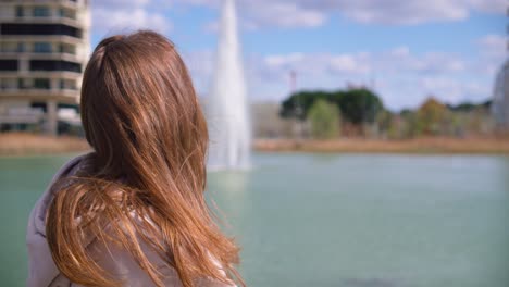 hermosa mujer morena disfrutando de un día soleado y mirando hacia la fuente, vista trasera