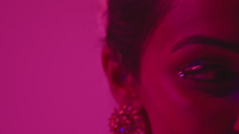 close up on face and jewellery of female kathak dancer performing dance wearing traditional indian dress against purple background