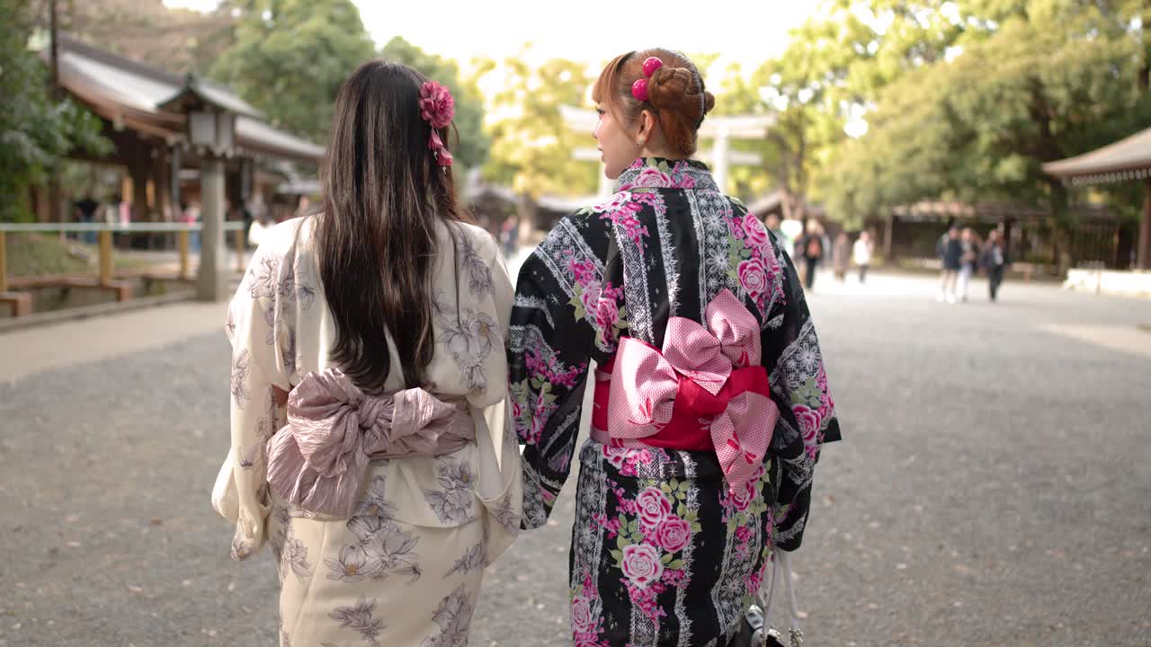 Cảnh nhìn từ phía sau của hai người phụ nữ mặc kimono họa tiết hoa đi bộ qua một đền thờ lịch sử của Nhật Bản