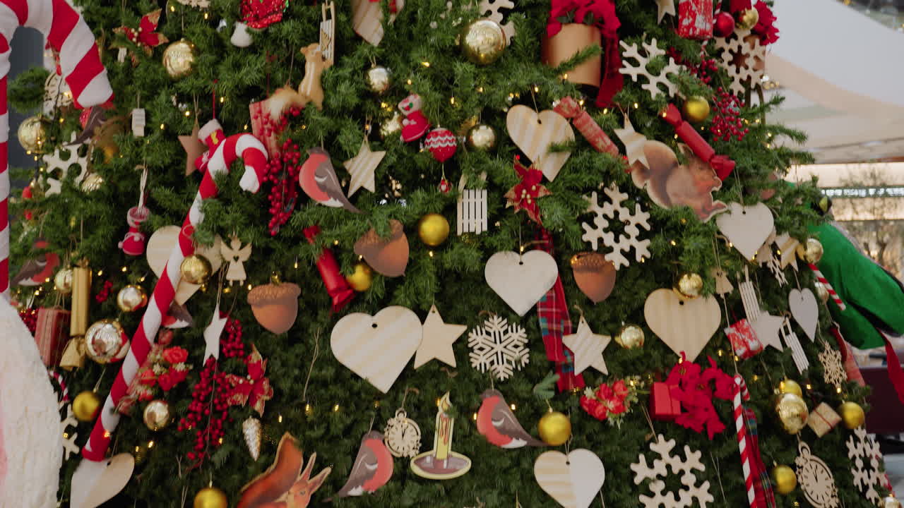 Close-up of tall Christmas tree adorned with ornaments and lights inside a festive shopping mall, holiday decorations fill the space, capturing a vibrant seasonal atmosphere